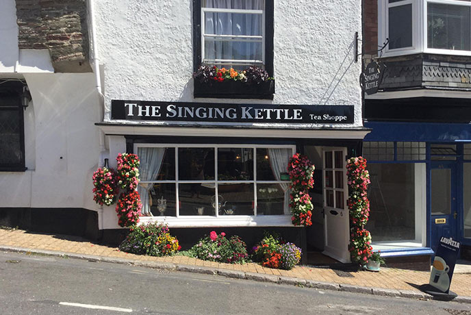 The quaint and traditional exterior of the Singing Kettle in Dartmouth, surrounded by flower pots and hanging baskets