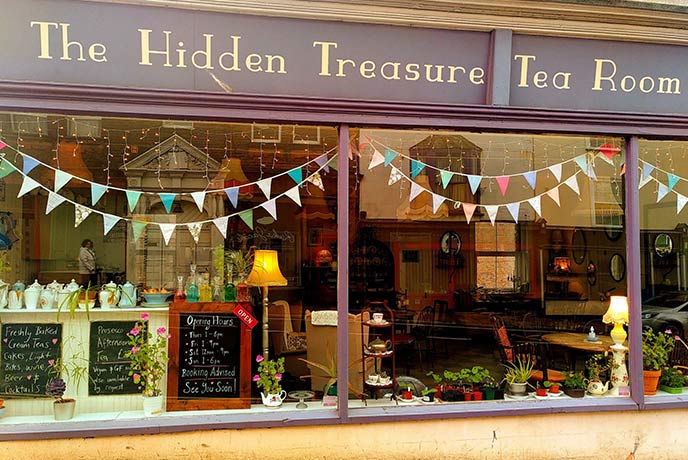 The window of The Hidden Treasure Tea Room with bunting hanging from the top and plants decorating the sill, home of one of the best afternoon teas in Devon