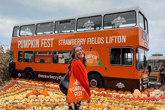 A person standing in front of an orange double decker bus surrounded by pumpkins at Pumpkin Fest at Strawberry Fields in Lifton