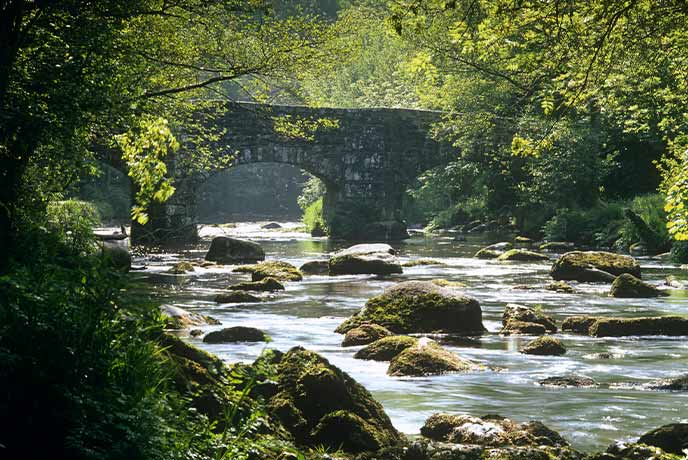 A beautiful stone bridge across a river and surrounded by trees in Teign Gorge near Castle Drogo in Dartmoor National Park