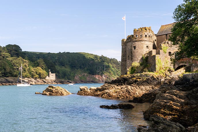 Dartmouth Castle sitting by the edge of the River Dart with a boat sailing past
