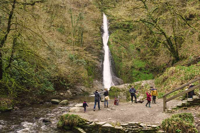 People standing at the viewing platform looking at the tumbling waterfall between the trees at Lydford Gorge in Dartmoor National Park