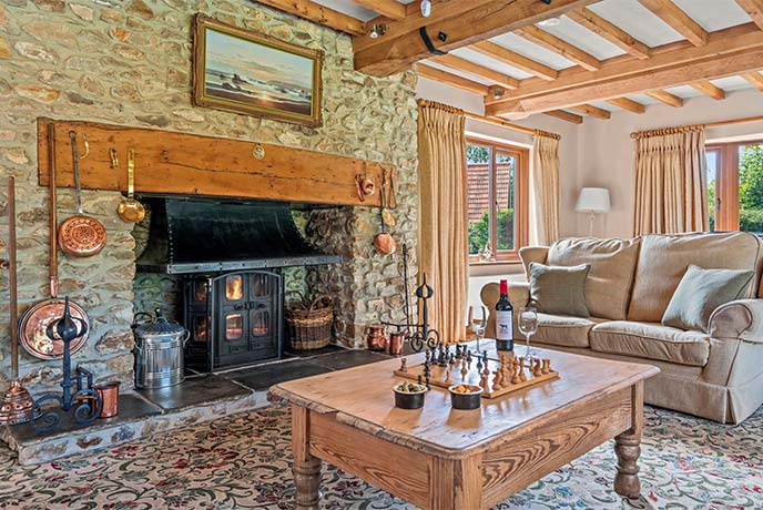 The cosy living room at Lexhayne Mill in Devon with beautiful expose stone walls and a lit wood-burner