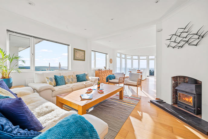 A bright and airy living room with a lit wood-burner and windows overlooking the sea at Seaview in Devon