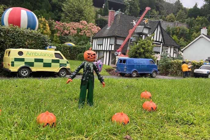 A tiny model village with a person jack-o'lanterns in the garden