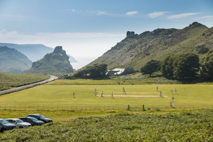 A field with the towering rock formations of the Valley of Rocks in the background