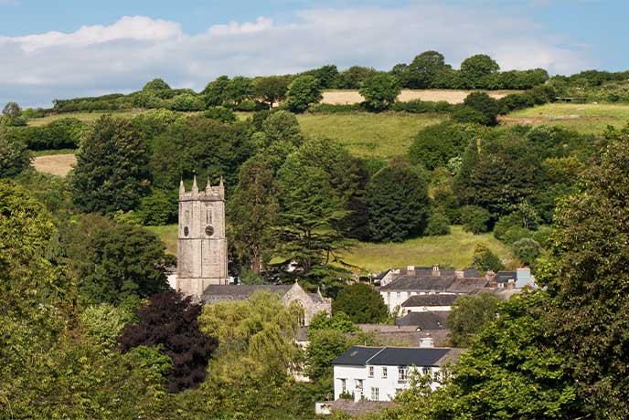 Looking through the trees at the pretty village of Ashburton in Dartmoor National Park, with a church and houses nestled in the rolling hills