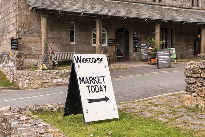A white A-board sign reading 'Widecombe Market' in Widecombe-in-the-Moor in Dartmoor National Park