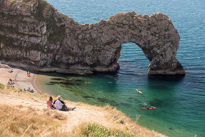 A couple sitting on the cliff above Durdle Door and the famous stone arch