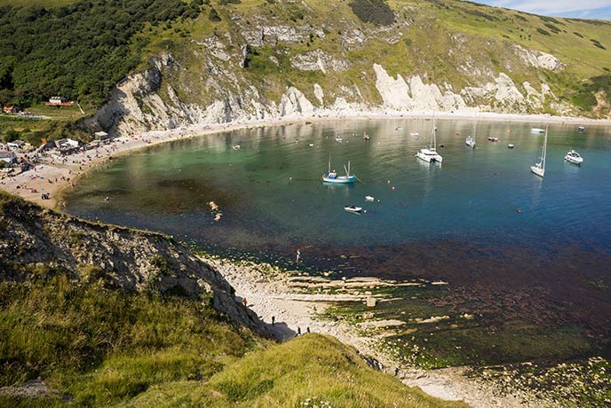 The basin like waters of Lulworth cove full of boats and people lounging on the sand