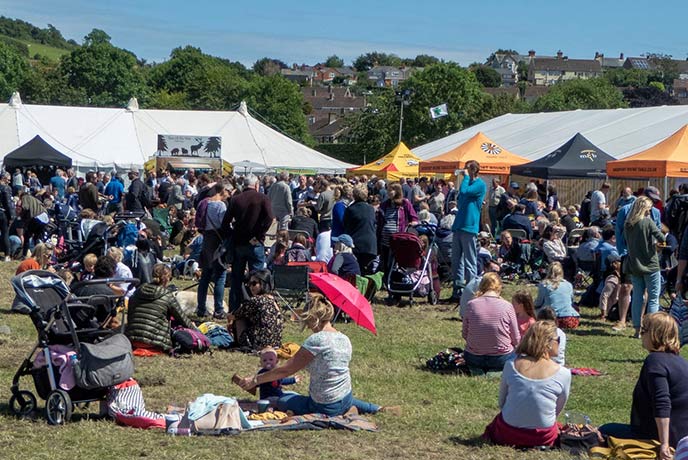People sat on the grass in front of the tents at Bridport Food Festival