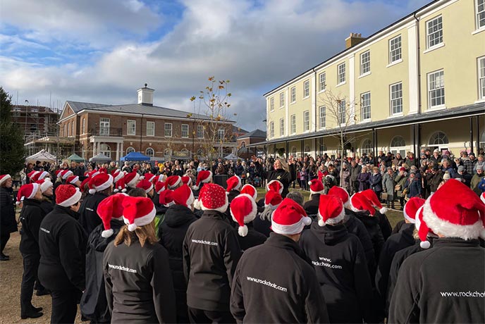 A group of people in santa hats singing at Poundbury Christmas Market in Dorset