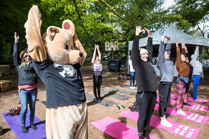 A group of people and someone in a bear costume doing yoga at Teddy Rocks Festival