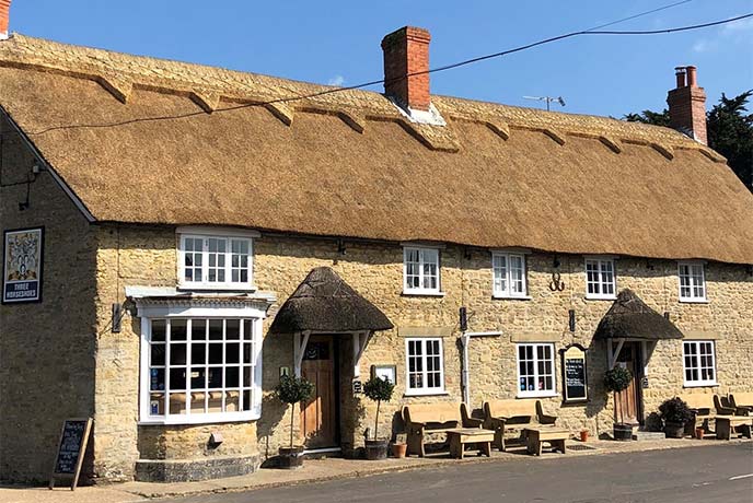 The traditional thatched exterior of The Three Horseshoes pub in Dorset