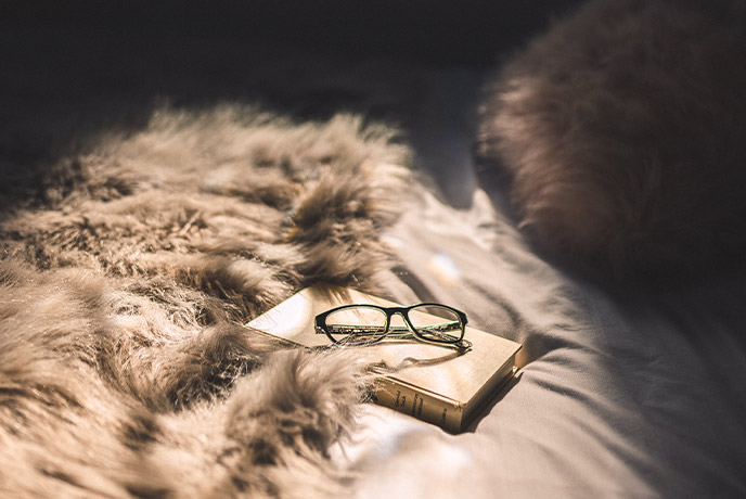 A book and a pair of reading glasses on a fur blanket at La Cabine Francaise in Dorset
