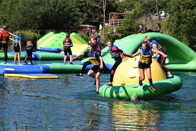 Children jumping into a lake from an inflatable obstacle course at Dorset Adventure Park