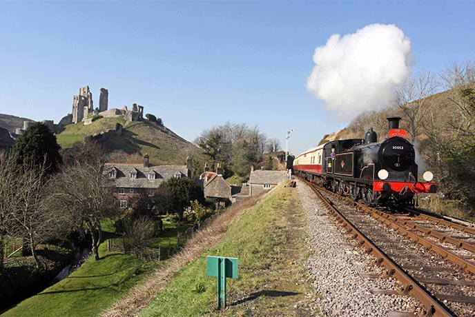 A black and red steam train running past Corfe Castle in Dorset with Swanage Railway