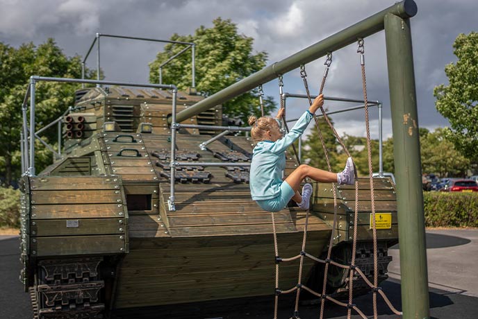 A child climbing up a rope on a tank in a play area at The Tank Museum in Dorset