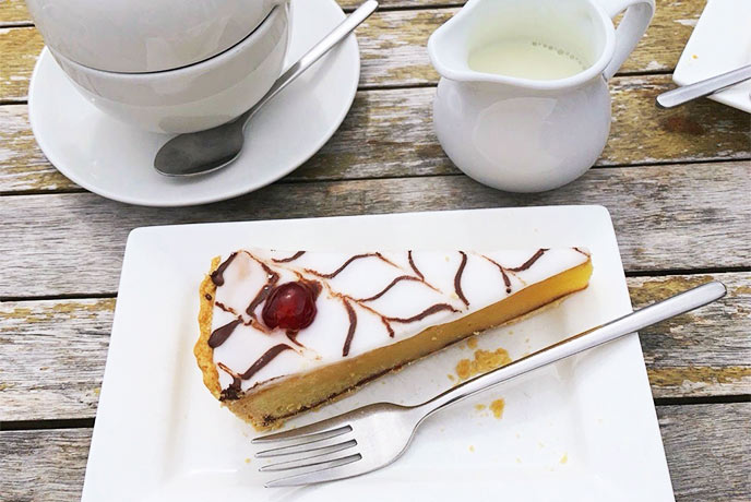 A slice of Bakewell Tart and a pot of tea on a wooden table