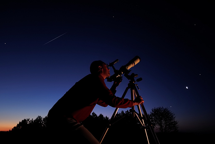 A man looking at the night sky through a telescope