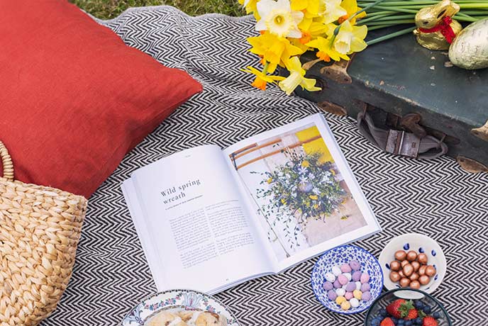 A picnic blanket covered in Easter treats, daffodils and cushions