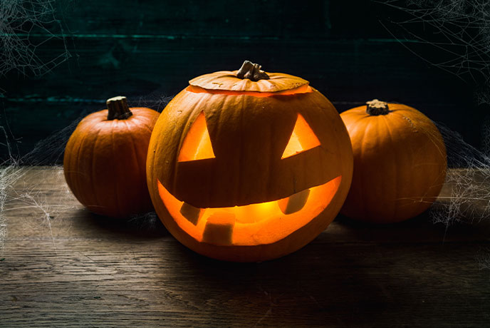 A carved pumpkin with a light inside next to two whole pumpkins