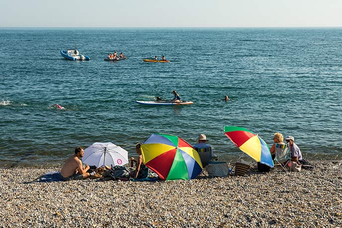 People relax on the beach at Freshwater Bay with umbrellas as people paddle past on boards