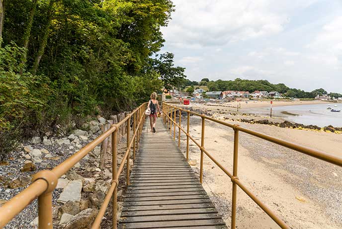 A person walking away from the camera along a wooden walkway above Seagrove Bay beach in Seaview