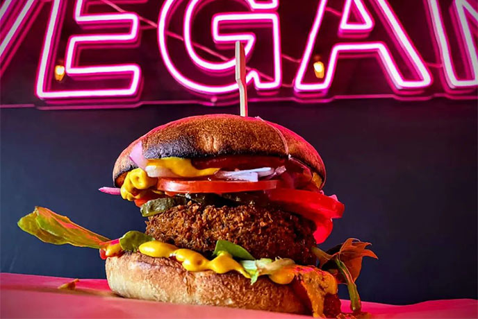 A vegan burger from Craft in front of a neon sign that says vegan