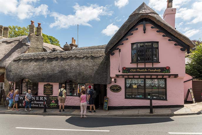 A thatched cottage with pink walls and people standing outside