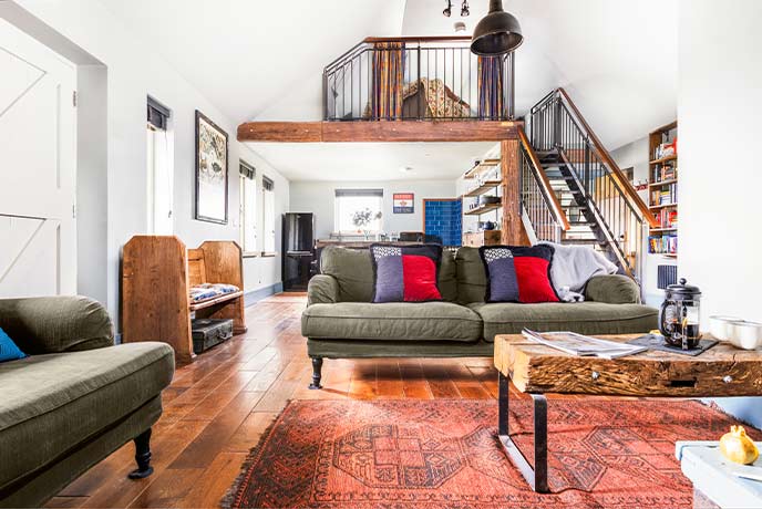 A cosy living room with wooden stairs behind leading to a mezzanine area at The Little Dairy Park Farm on the Isle of Wight