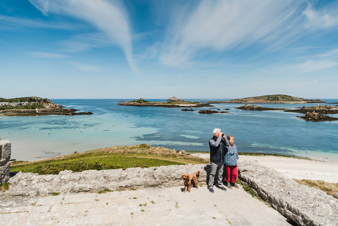 A couple and their dog looking out at the views with the sea and islands behind them.