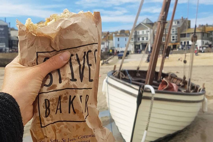 Someone holding a pasty from St Ives Bakery in front of a boat