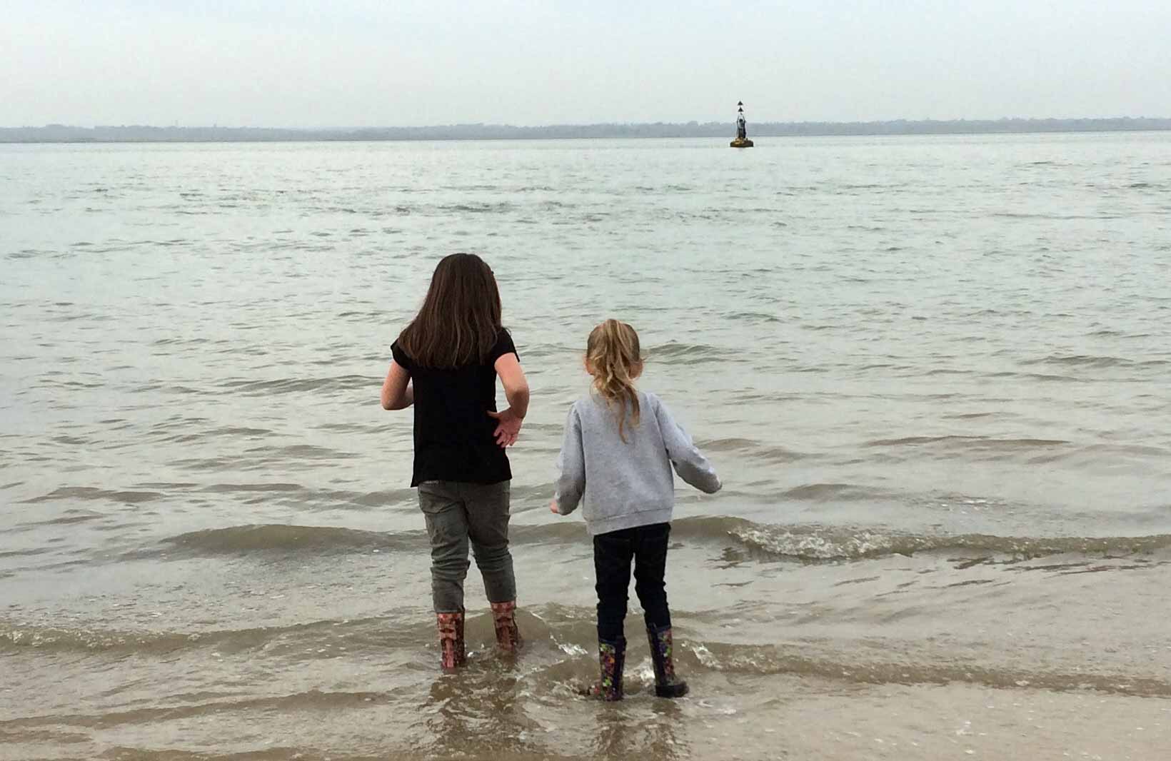 Two little girls wash their muddy wellies while looking out to sea next to Fort Victoria on the Isle of Wight.