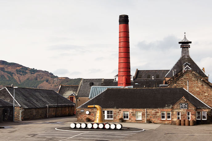 The famous Balblair Distillery with barrels out front and a towering red chimney in the background