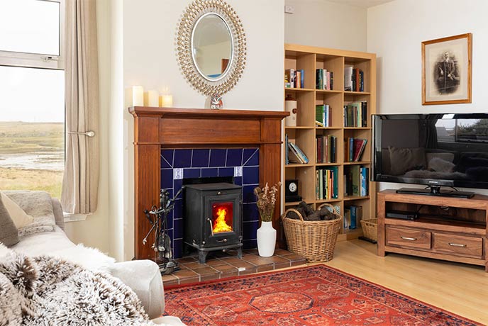 The cosy living room at Stella Maris with a lit wood-burner and bookshelves full of books