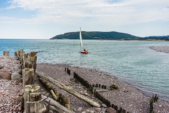 Looking out over the shingle beach at Porlock Weir as a little boat floats across the sea