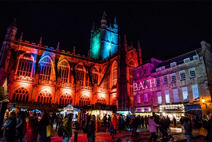 Bath Abbey lit up with colourful lights above the Bath Christmas Market