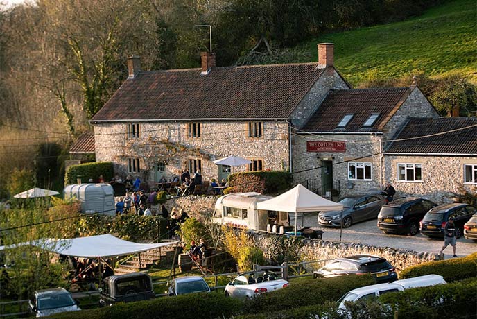 The traditional stone exterior of The Cotley Inn in Somerset, with outdoor seating and fields behind