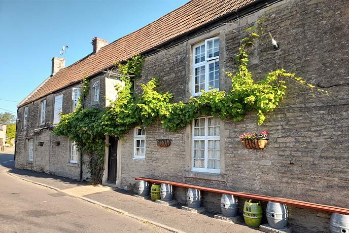 The stone exterior of The White Hart pub in Somerset with creeping plants growing along the walls