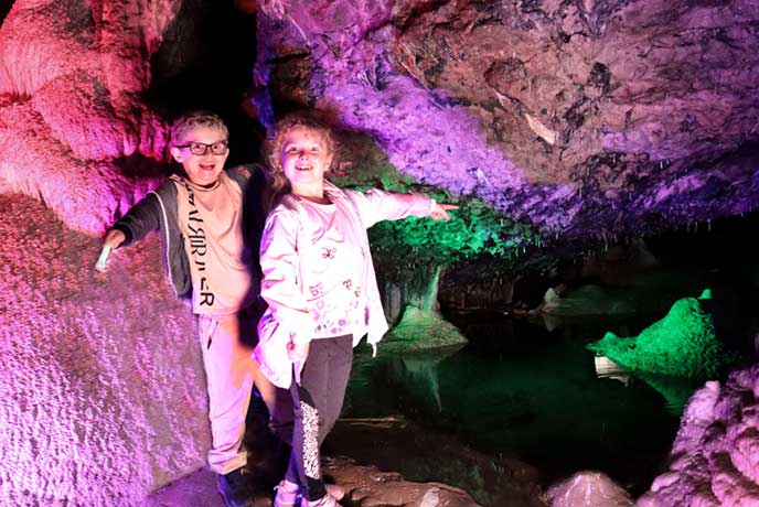 Two children standing in the colourfully illuminated caves at Wookey Hole in Somerset