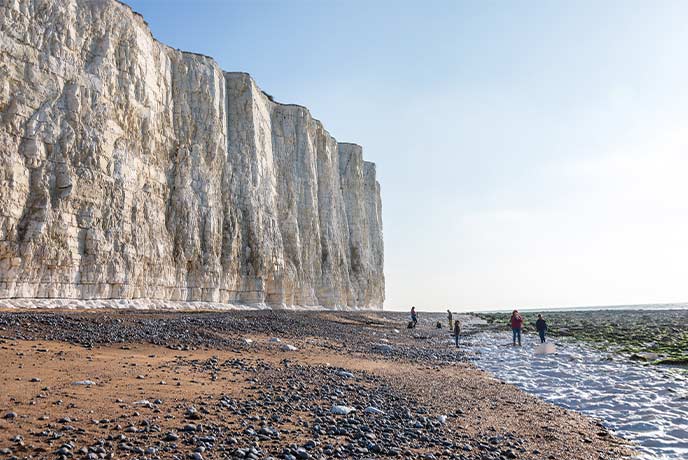 People on the golden beach beneath the towering chalk cliffs along the Birling Gap in Sussex