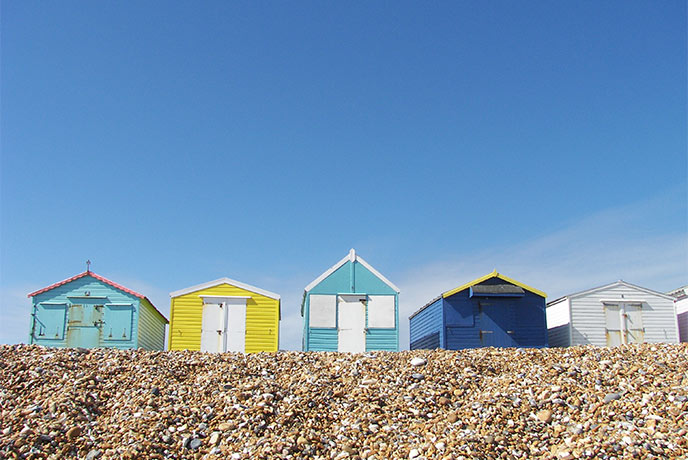 A selection of colourful beach huts above the shingle sands of Bulverhythe beach in East Sussex