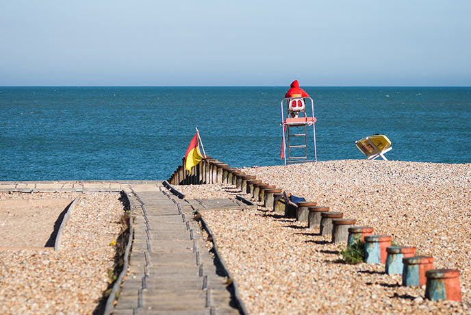 A track leading down Eastbourne beach where a lifeguard sits on top of a chair in front of the sea