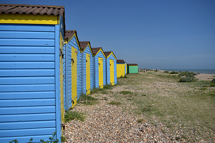 Looking down a row of bright blue beach huts with yellow doors at Littlehampton beach