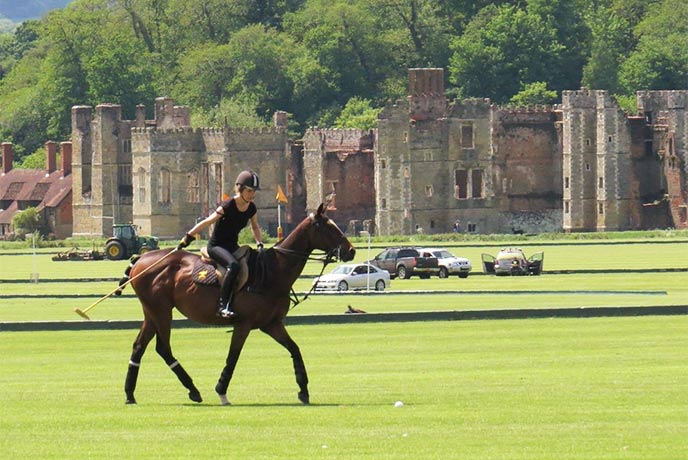 Someone practicing polo on a horse at Cowdray Park Polo Club Academy with the ruins of Cowdray Castle in the background