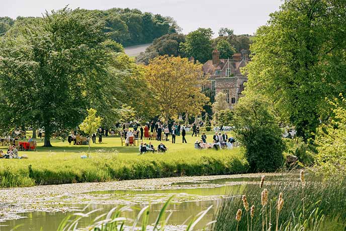 Looking across some water at the historic Glyndebourne House with people on the lawn for the Glyndebourne Festival