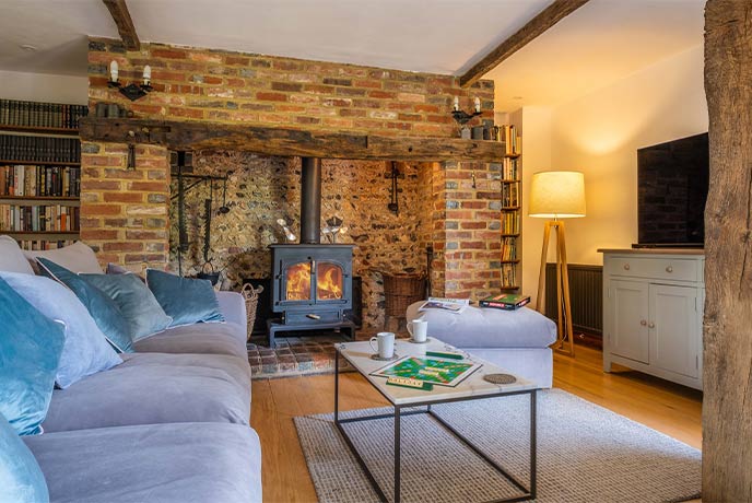 The cosy living room at Acorn Barn in Sussex with a lit wood-burner and expose brick walls