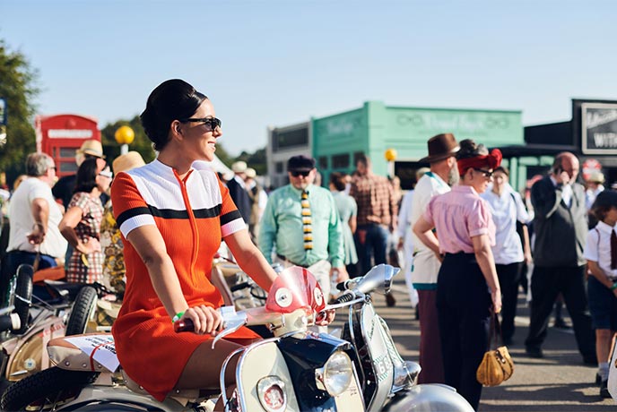 Someone in vintage 60s clothes sat on a vintage bike at the Goodwood Revival festival in Sussex