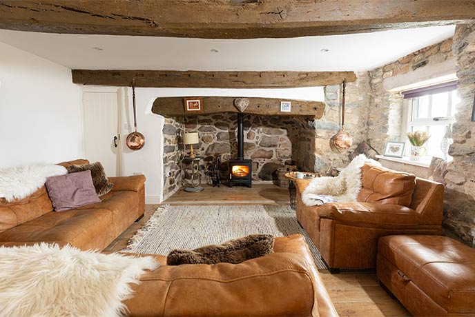 The cosy living room at Bwlch Y Groes in Gwynedd with exposed stone walls, leather sofas and a lit wood-burner